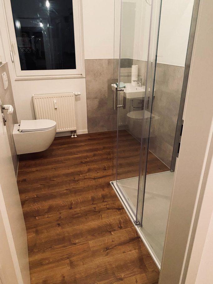 Modernes Badezimmer mit Dusche, WC und Holzfußboden.