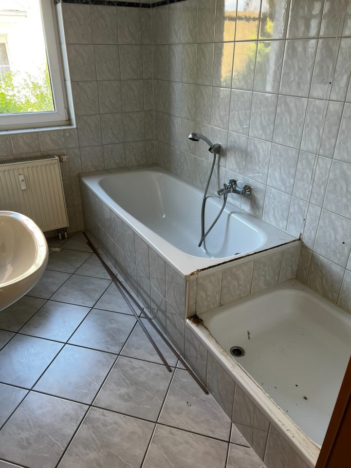 Heller Badezimmerbereich mit Badewanne, Dusche und Fliesenboden.