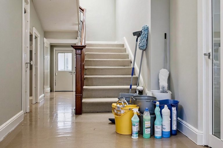 Hausmeisterdienst. Reinigungsservice. Reinigung. Wohnungsservice Reinigungsmittel und Utensilien stehen vor einer Treppe in einem hellen Flur.